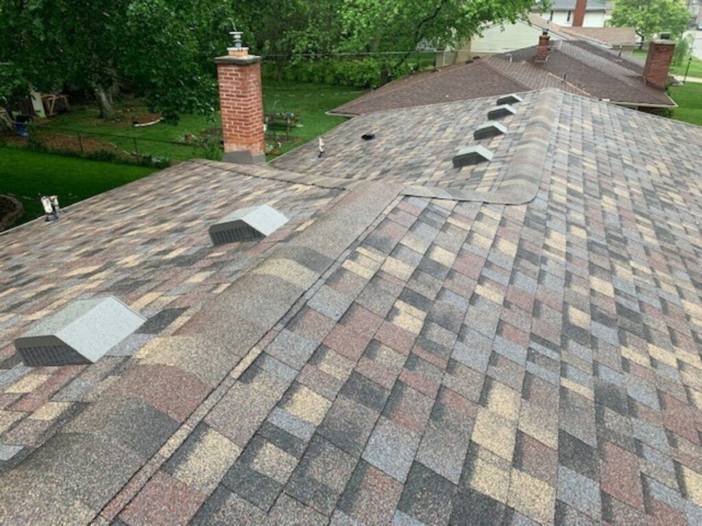 A close-up of a residential roof with decorative herringbone asphalt shingles in various colors.