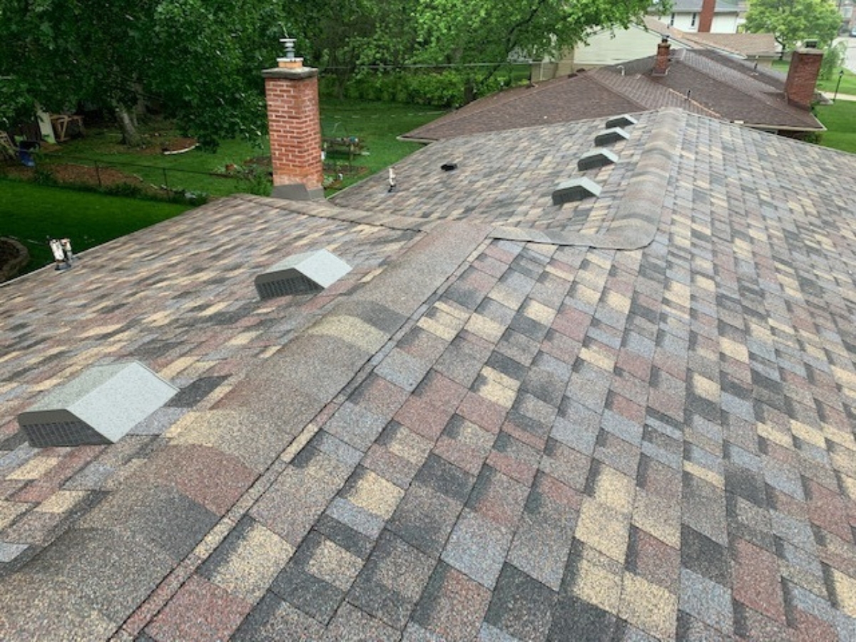 A close-up of a residential roof with decorative herringbone asphalt shingles in various colors.