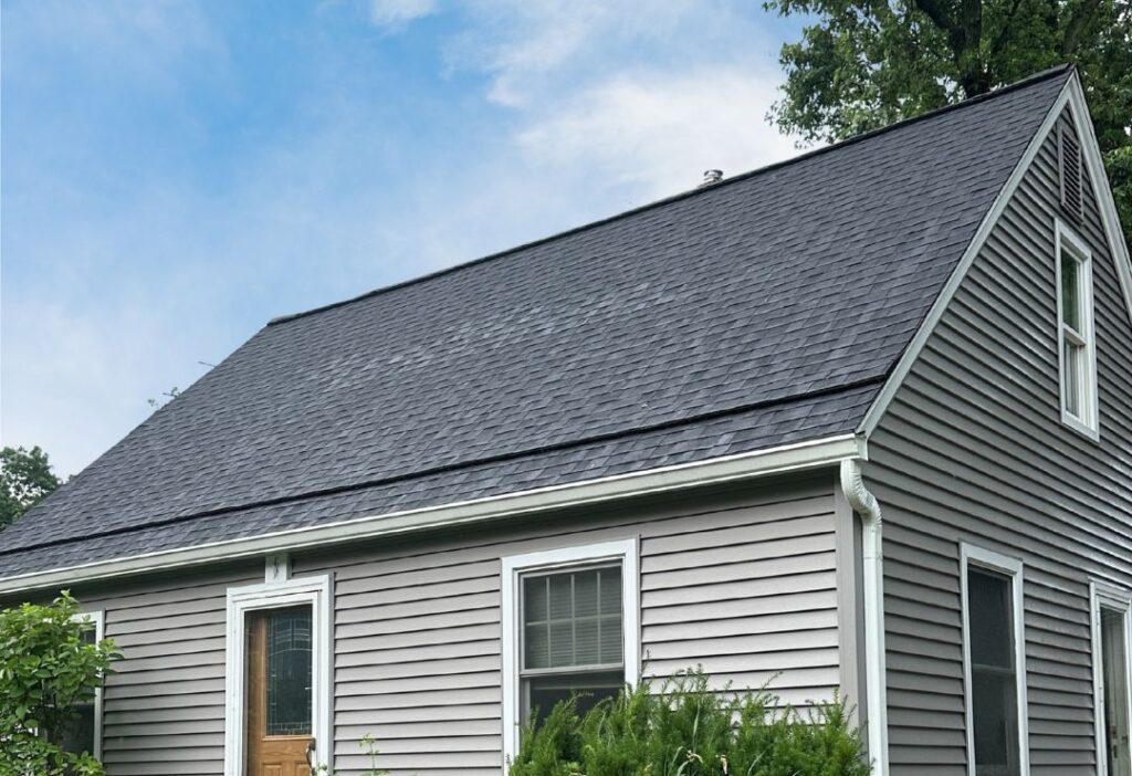 Modern residential building with sleek dark shingles and light grey siding, surrounded by lush greenery. Ann Arbor Roof Replacement Featuring Owens Corning Duration Onyx Black Shingles