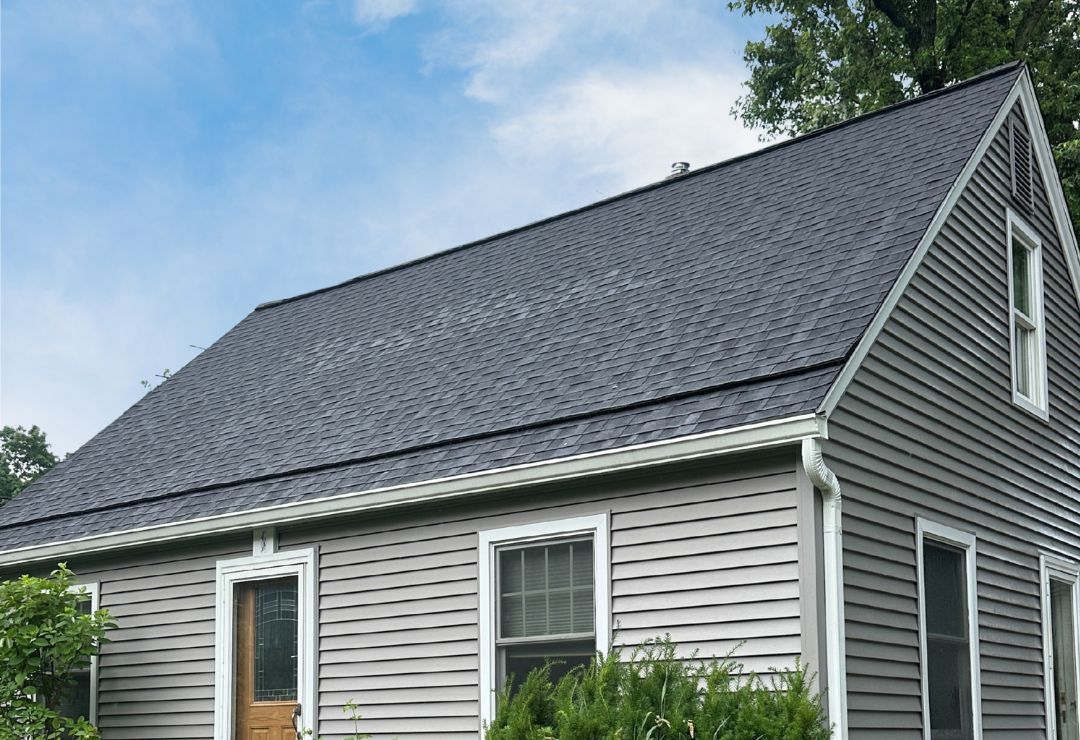 Modern residential building with sleek dark shingles and light grey siding, surrounded by lush greenery. Ann Arbor Roof Replacement Featuring Owens Corning Duration Onyx Black Shingles