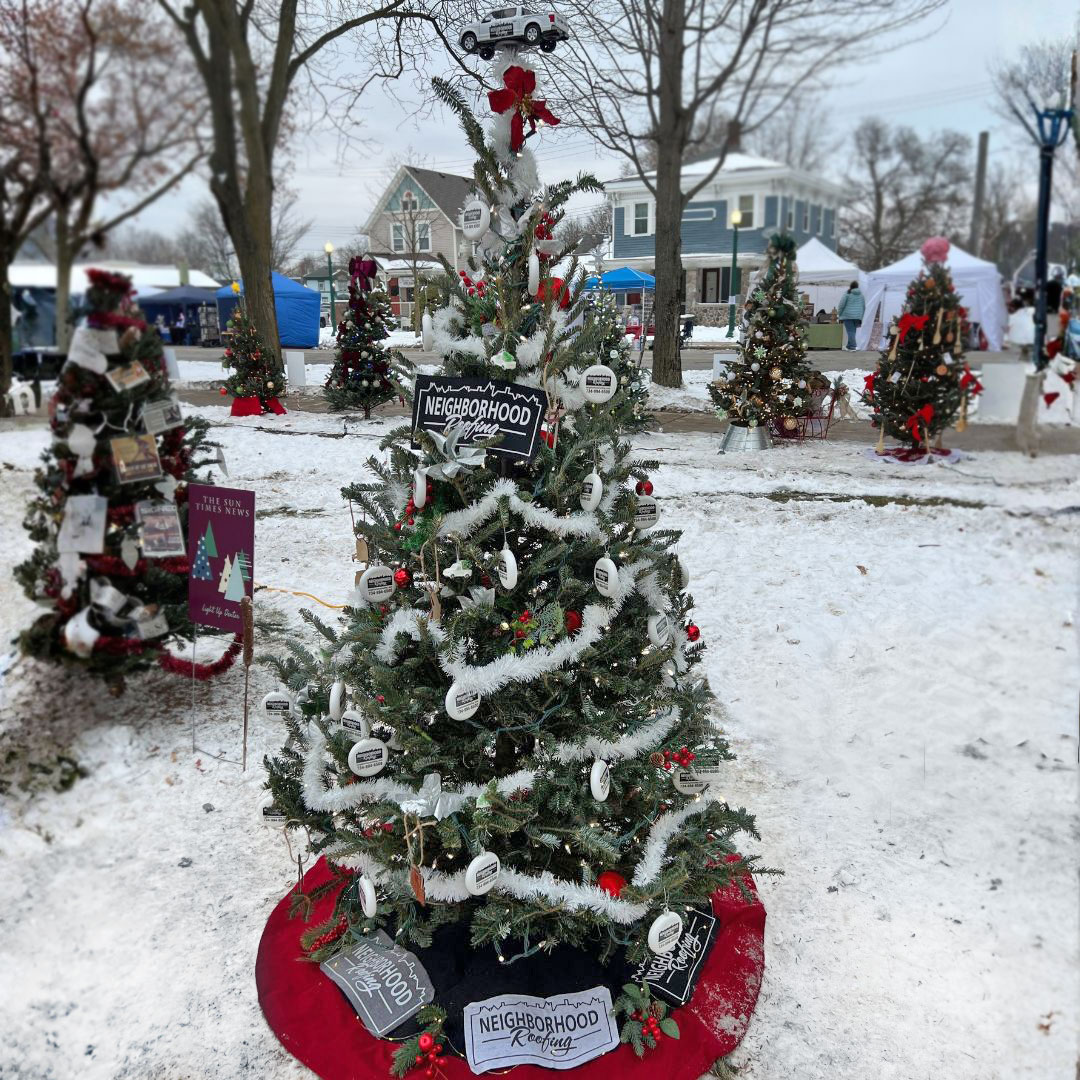 Festively decorated Christmas trees highlight neighborhood pride and local businesses in a snowy winter scene.