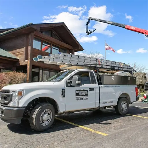 Neighborhood Roofing work truck parked in front of a modern wooden building on a sunny day.